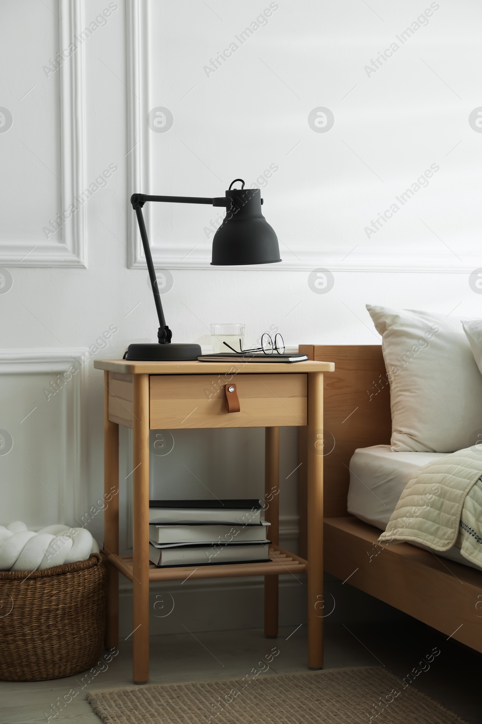 Photo of Bedside table with lamp, notebook, glasses, books and glass of water near bed indoors