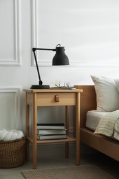 Photo of Bedside table with lamp, notebook, glasses, books and glass of water near bed indoors