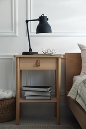 Photo of Bedside table with lamp, notebook, glasses, books and glass of water near bed indoors