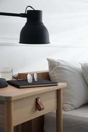 Photo of Bedside table with lamp, notebook, glasses and glass of water near bed indoors, closeup