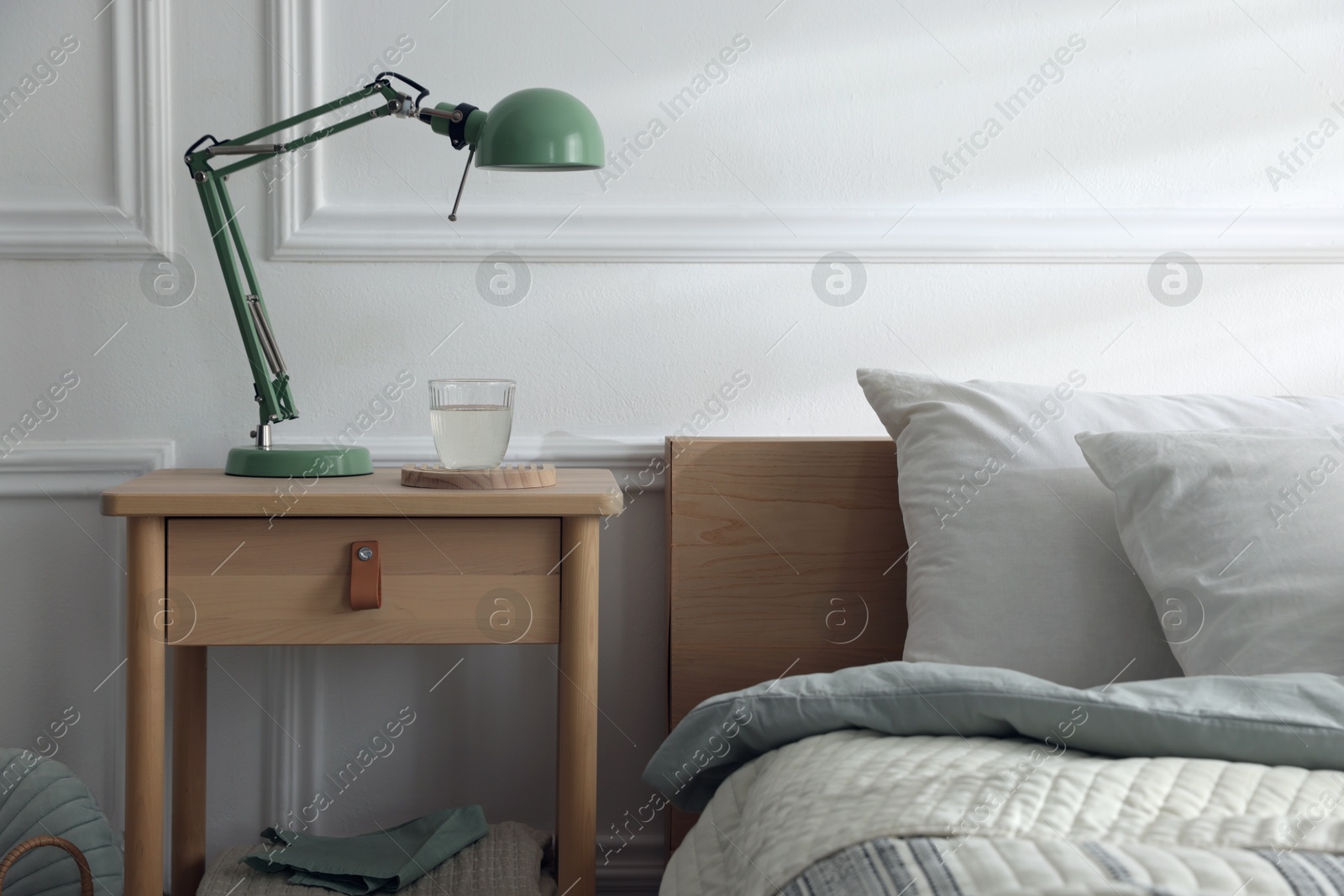 Photo of Bedside table with lamp and glass of water near bed indoors