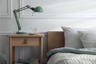 Photo of Bedside table with lamp and glass of water near bed indoors