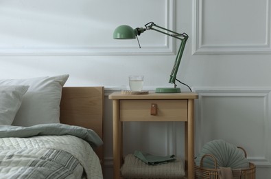 Photo of Bedside table with lamp and glass of water near bed indoors