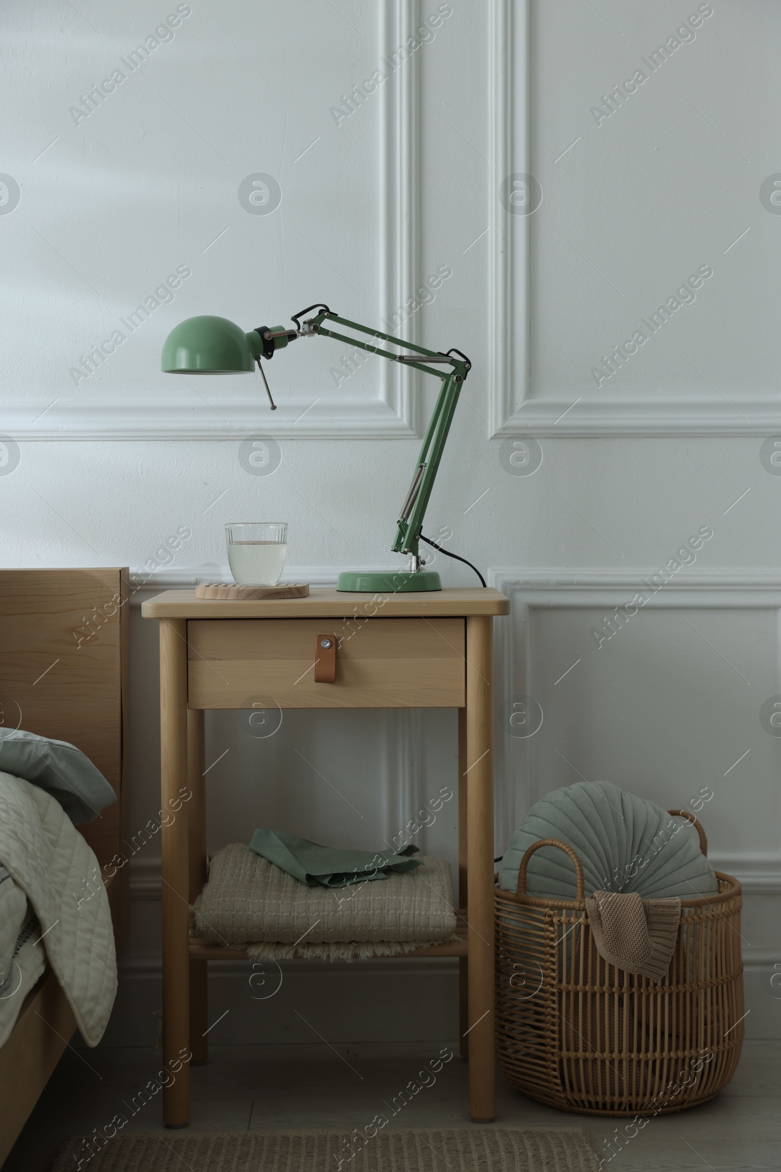 Photo of Bedside table with lamp and glass of water near bed indoors