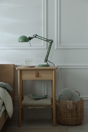 Photo of Bedside table with lamp and glass of water near bed indoors