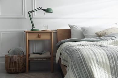 Photo of Bedside table with lamp and glass of water near bed indoors