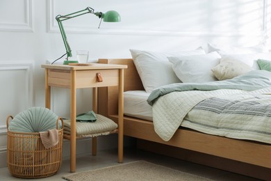 Photo of Bedside table with lamp and glass of water near bed indoors