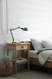 Photo of Bedside table with lamp and glass of water near bed indoors
