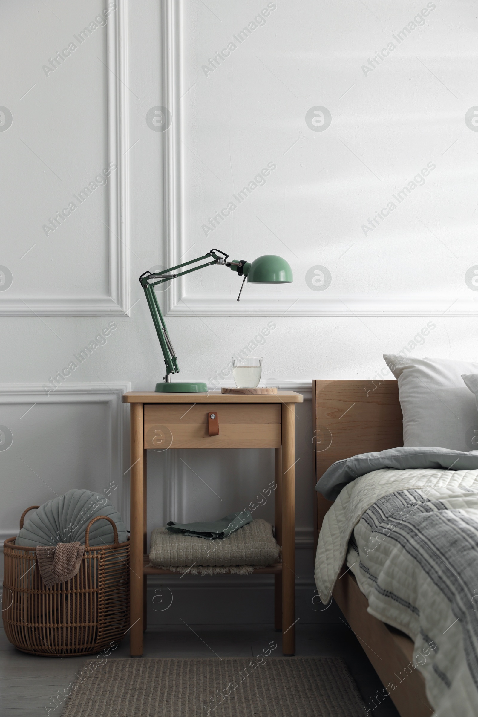 Photo of Bedside table with lamp and glass of water near bed indoors