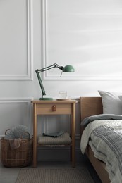 Photo of Bedside table with lamp and glass of water near bed indoors