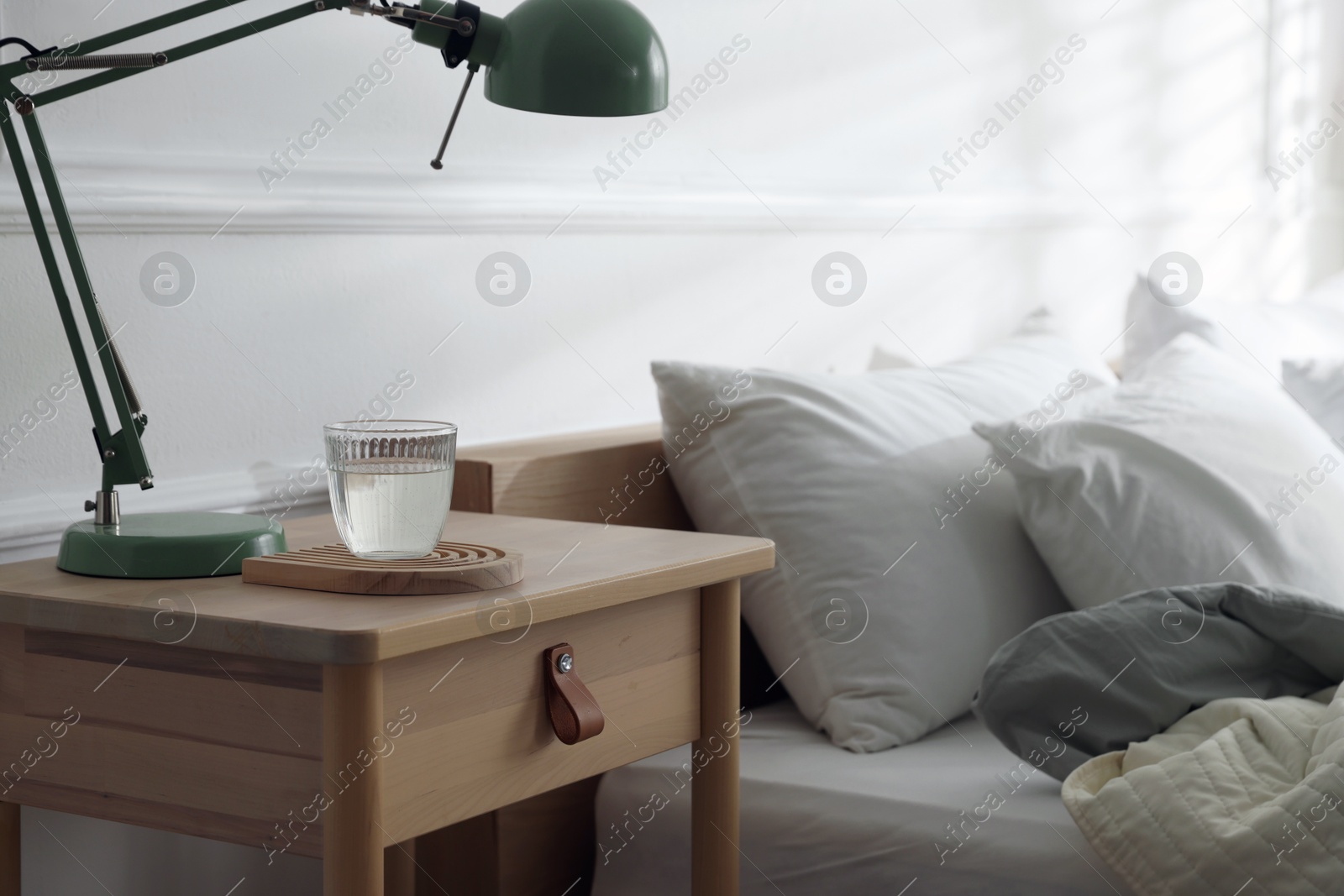 Photo of Bedside table with lamp and glass of water near bed indoors
