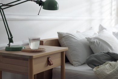 Photo of Bedside table with lamp and glass of water near bed indoors