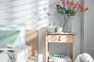 Photo of Bedside table with different decor near bed indoors