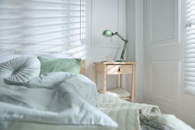 Photo of Bedside table with lamp and glass of water near bed indoors