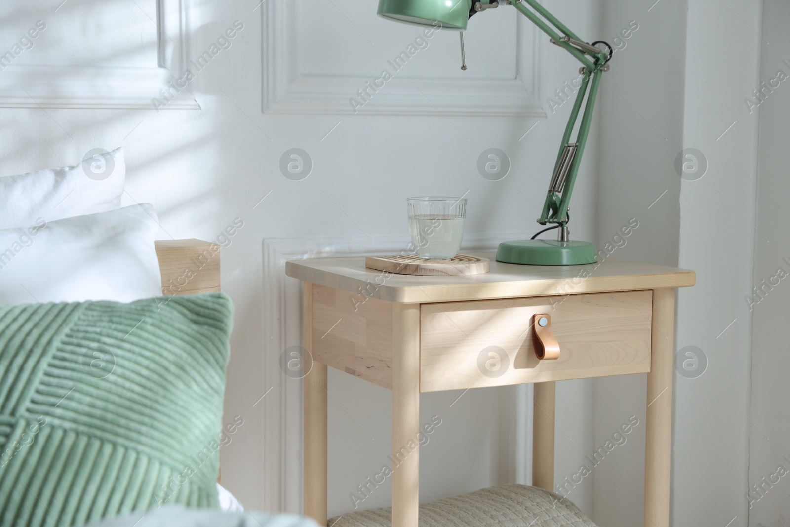 Photo of Bedside table with lamp and glass of water near bed indoors