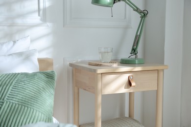 Photo of Bedside table with lamp and glass of water near bed indoors