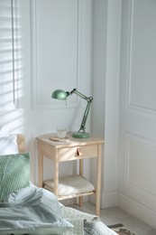 Photo of Bedside table with lamp and glass of water near bed indoors