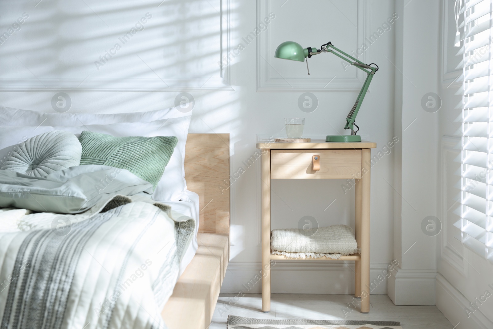 Photo of Bedside table with lamp and glass of water near bed indoors