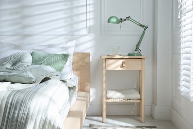 Photo of Bedside table with lamp and glass of water near bed indoors