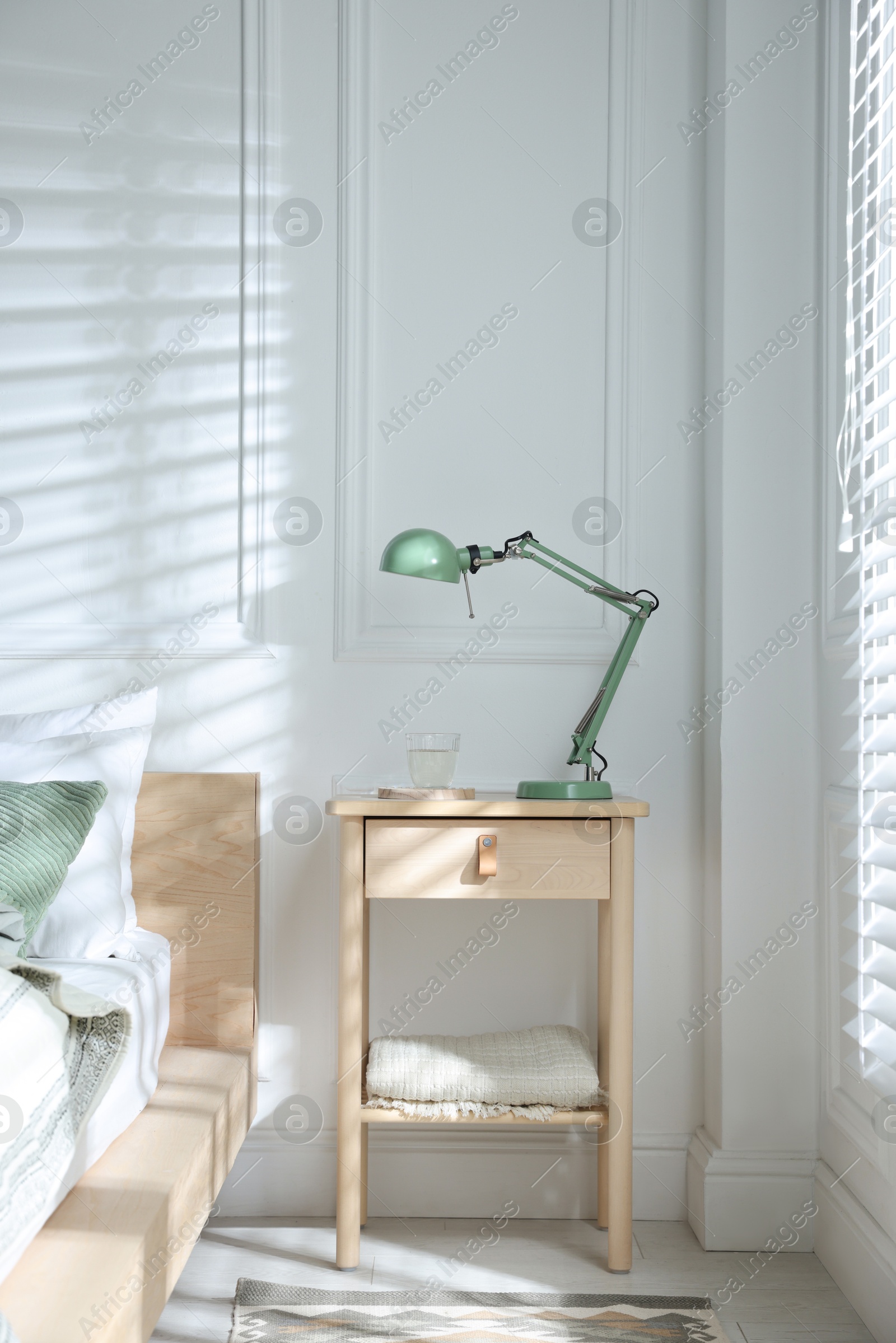 Photo of Bedside table with lamp and glass of water near bed indoors