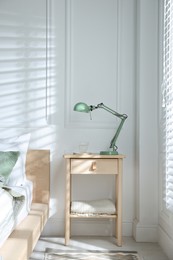 Photo of Bedside table with lamp and glass of water near bed indoors