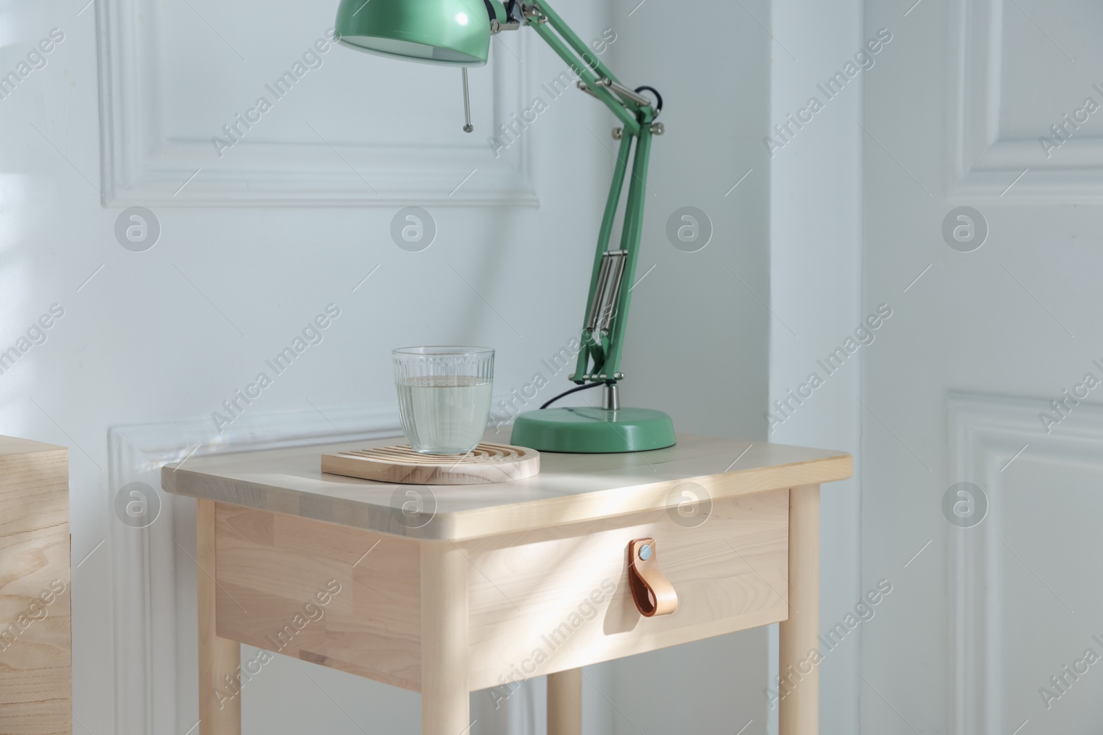 Photo of Bedside table with lamp and glass of water indoors
