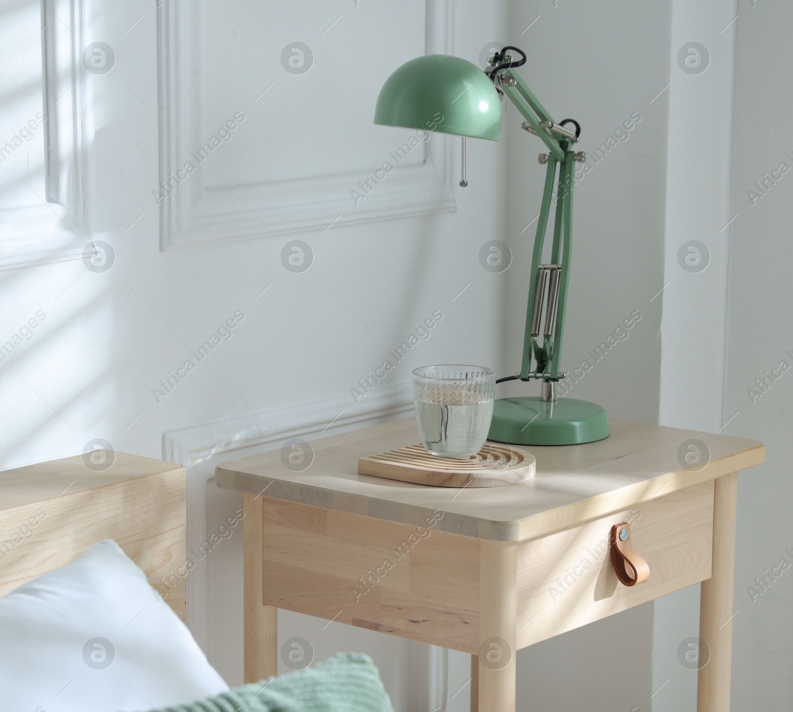 Photo of Bedside table with lamp and glass of water near bed indoors