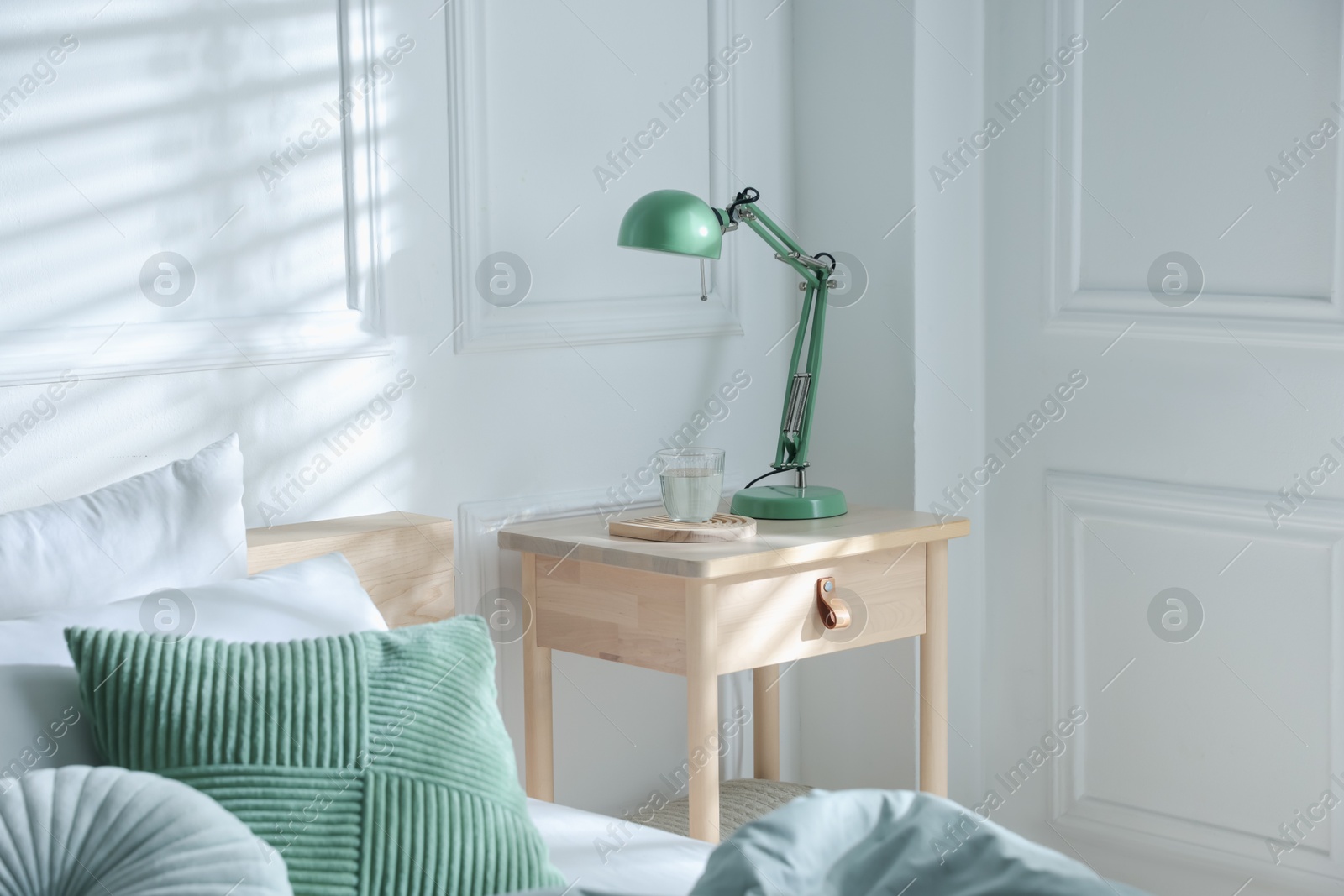 Photo of Bedside table with lamp and glass of water near bed indoors