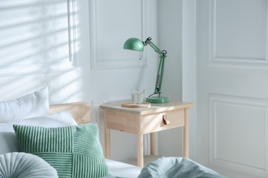 Photo of Bedside table with lamp and glass of water near bed indoors