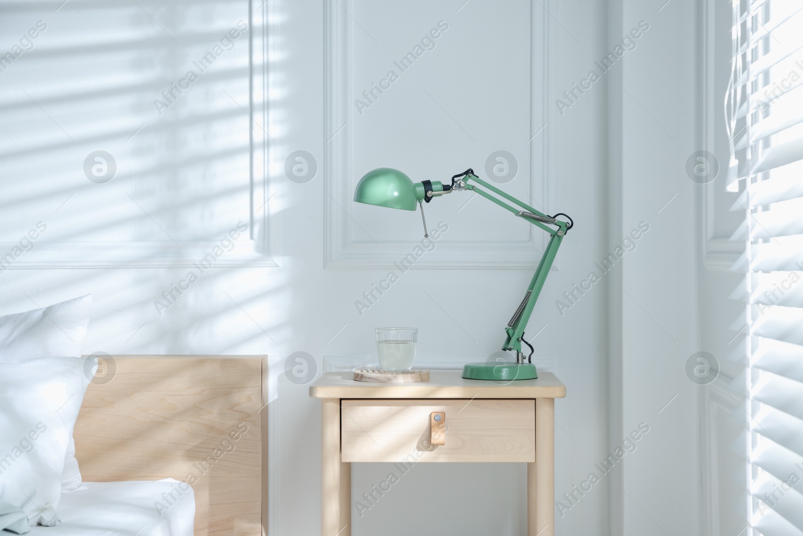 Photo of Bedside table with lamp and glass of water near bed indoors