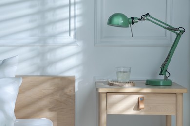 Photo of Bedside table with lamp and glass of water near bed indoors