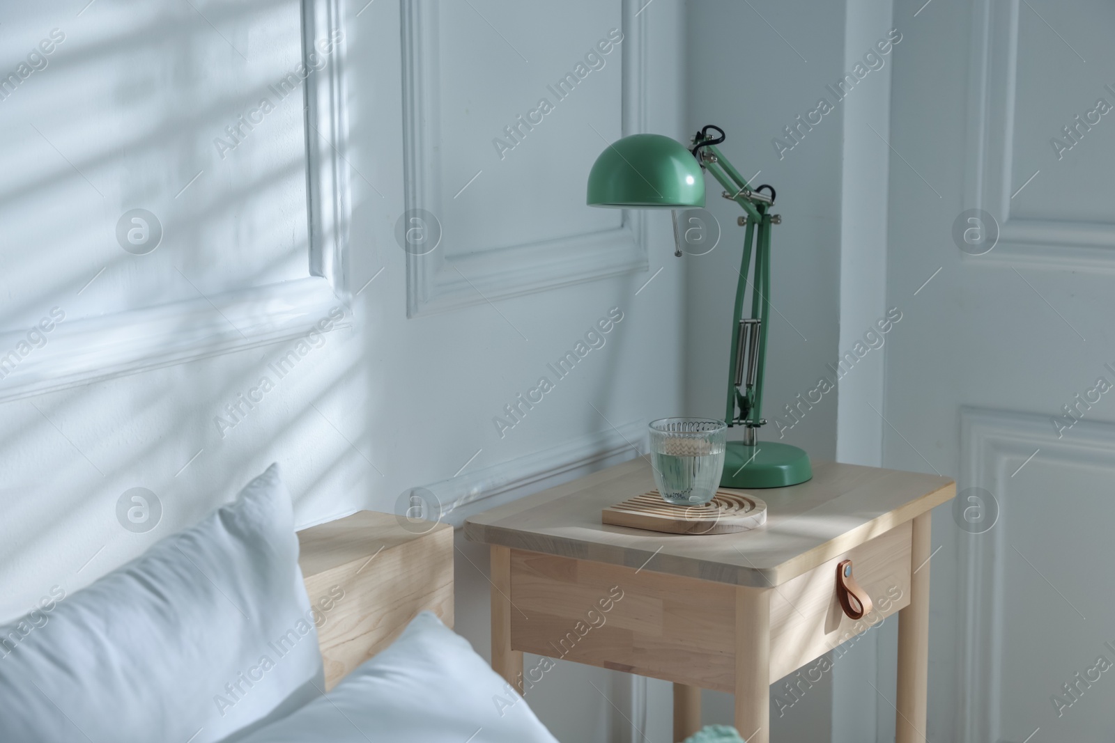 Photo of Bedside table with lamp and glass of water near bed indoors