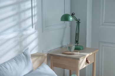 Photo of Bedside table with lamp and glass of water near bed indoors