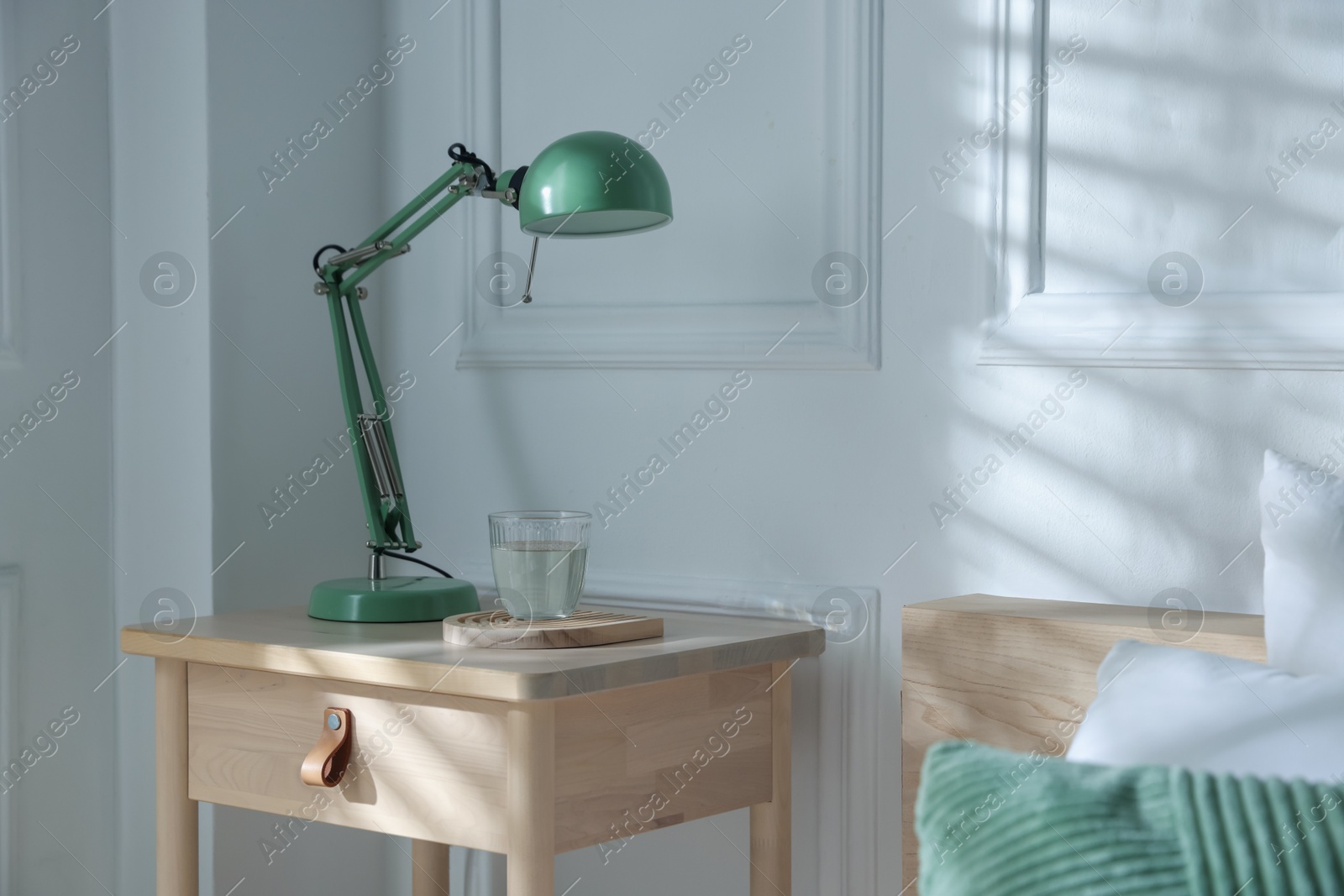 Photo of Bedside table with lamp and glass of water near bed indoors