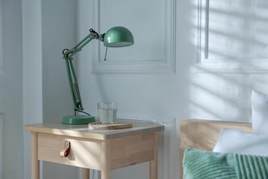 Photo of Bedside table with lamp and glass of water near bed indoors