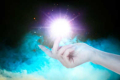 Image of Woman creating bright light in smoke against black background, closeup. Aura, spiritual practice