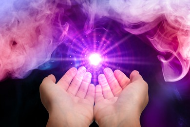 Image of Woman creating bright light in smoke against black background, closeup. Aura, spiritual practice