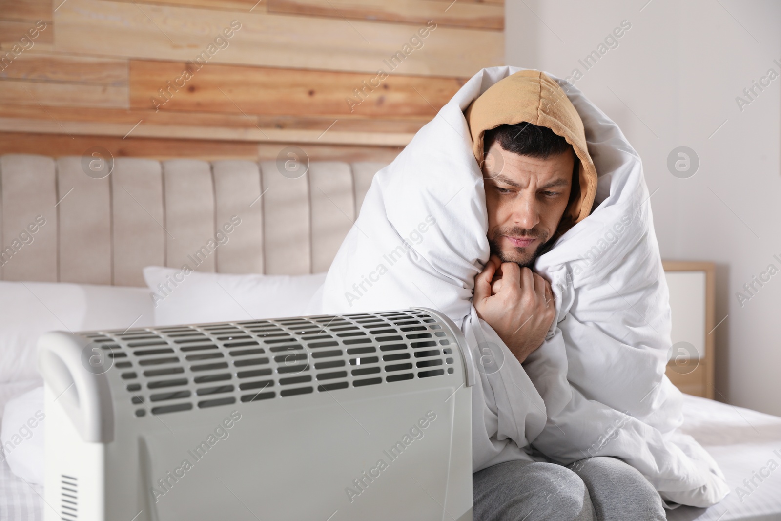 Man sitting in bed near electric heater at home Photo of Man sitting in bed near electric heater at home