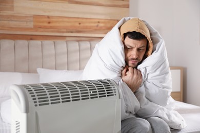 Photo of Man sitting in bed near electric heater at home