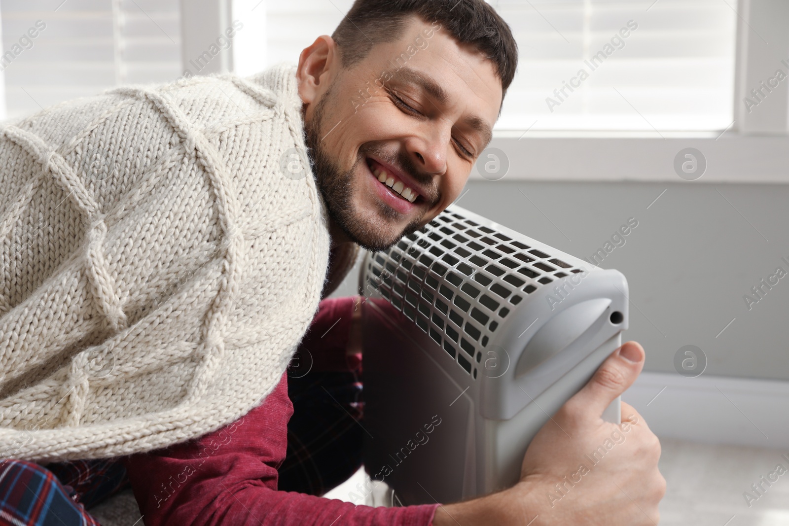Photo of Man with blanket warming near electric heater at home