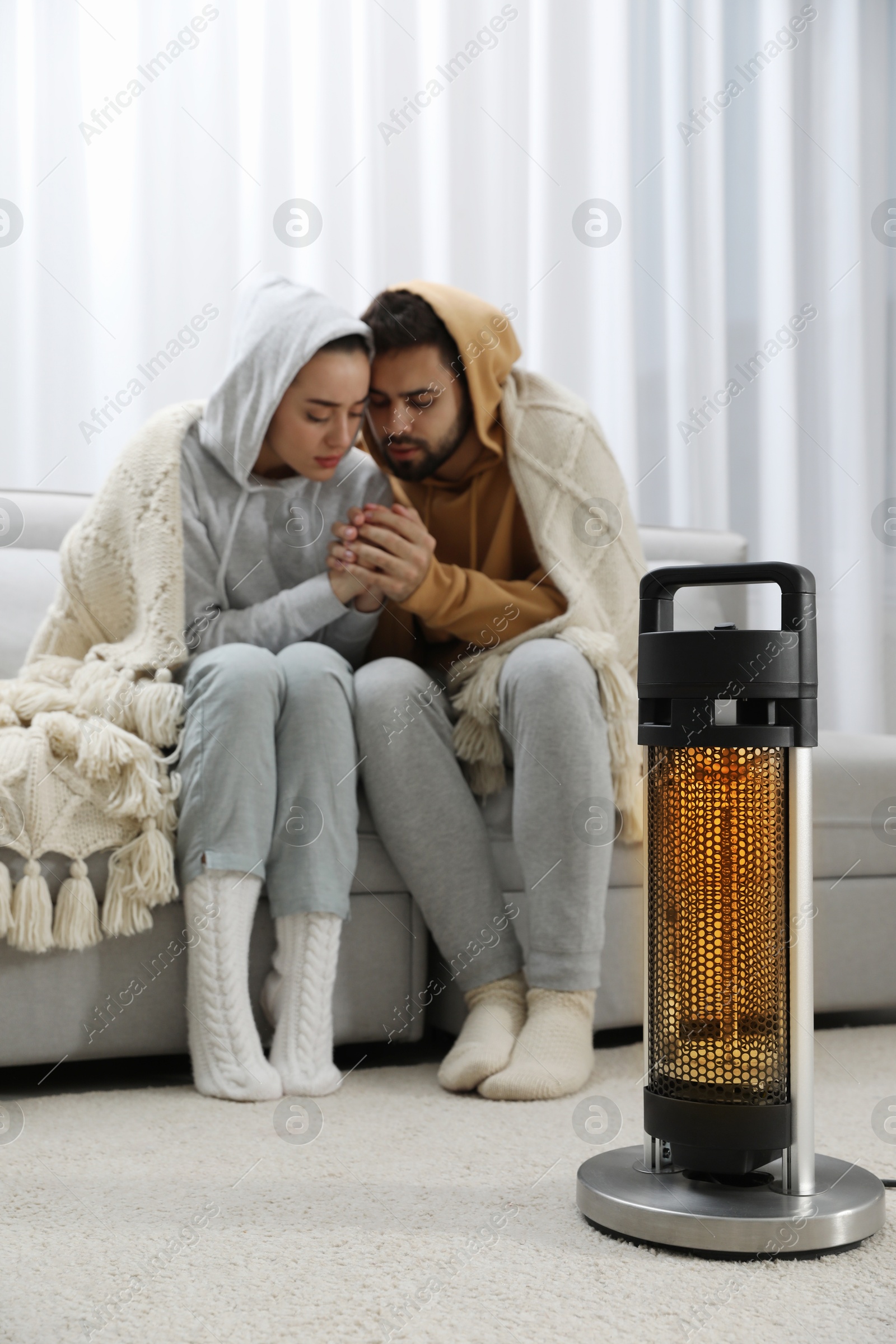 Young couple getting warm near electric heater at home Photo of Young couple getting warm near electric heater at home