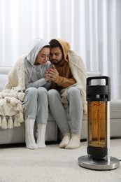 Photo of Young couple getting warm near electric heater at home