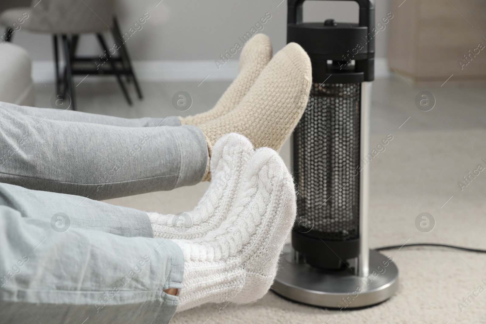 Photo of Couple in socks warming feet near electric heater at home, closeup