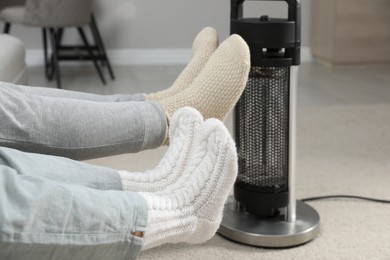 Photo of Couple in socks warming feet near electric heater at home, closeup
