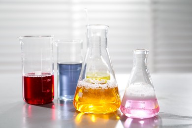 Photo of Laboratory glassware with different samples on light table indoors, closeup. Solution chemistry