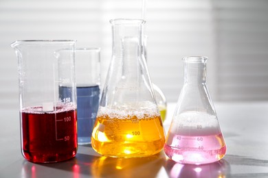 Photo of Laboratory glassware with different samples on light table indoors, closeup. Solution chemistry