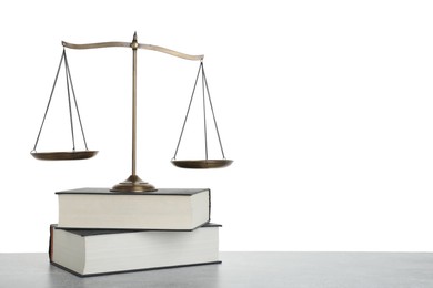 Photo of Golden scales of justice and books on light grey table against white background
