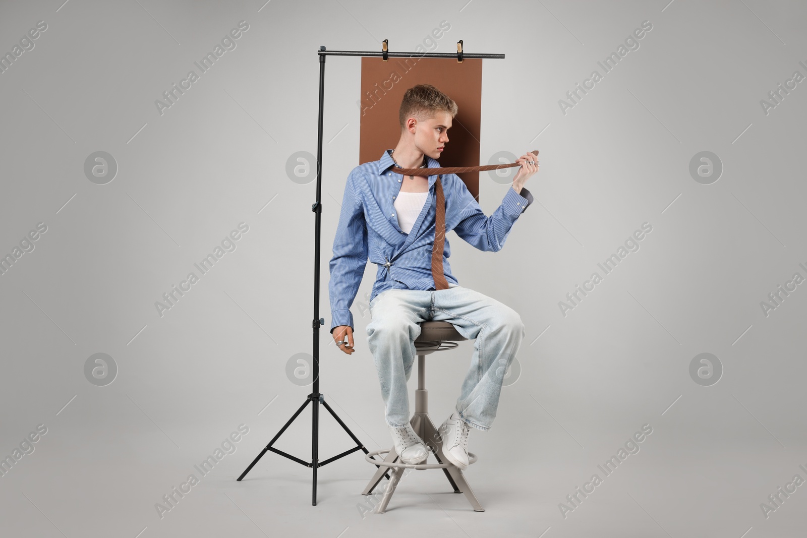 Photo of Handsome young man wearing stylish clothes sitting on chair against light grey background
