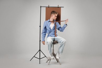 Photo of Handsome young man wearing stylish clothes sitting on chair against light grey background