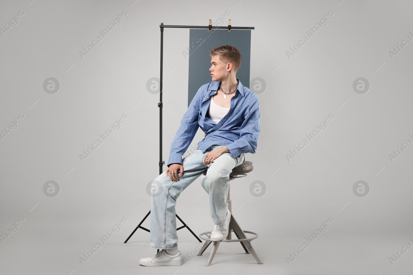 Photo of Handsome young man wearing stylish clothes sitting on chair against light grey background